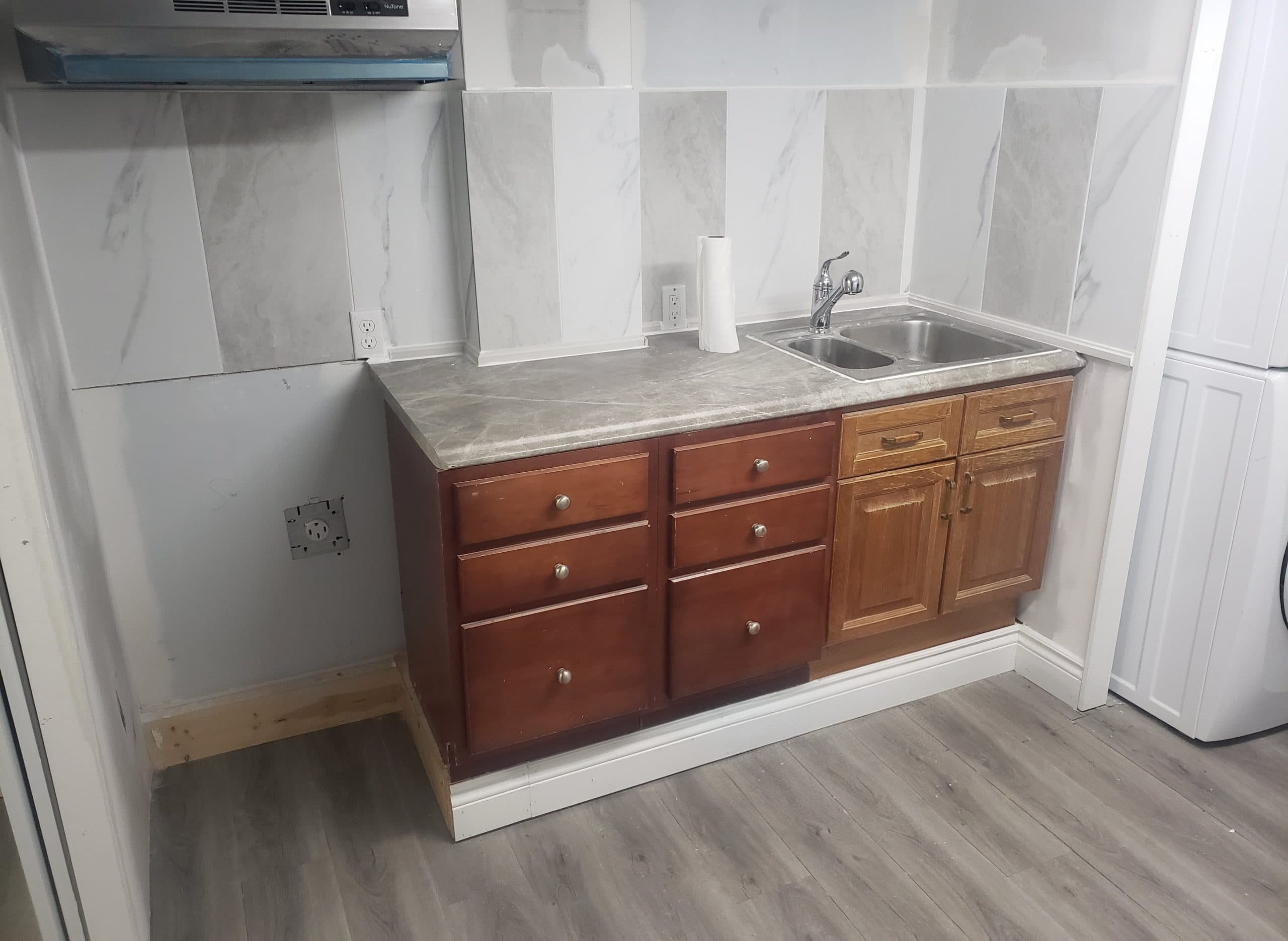 Completed kitchenette with cabinetry, sink, countertop, and range hood